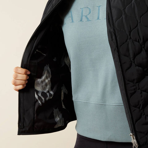 Woman wearing a black quilted vest over a light blue long-sleeve shirt on a beige background