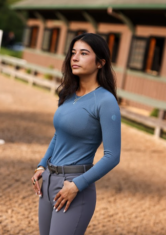 Person wearing a blue long-sleeve top and navy pants with a gold belt on a light gray background