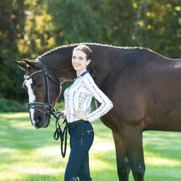 A person standing next to a horse in a field, wearing riding apparel.