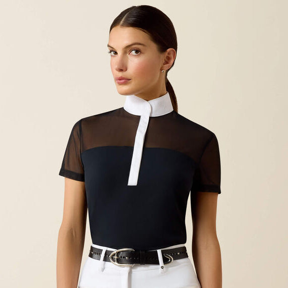 Woman wearing a black and white top with sheer sleeves and white pants on a beige background