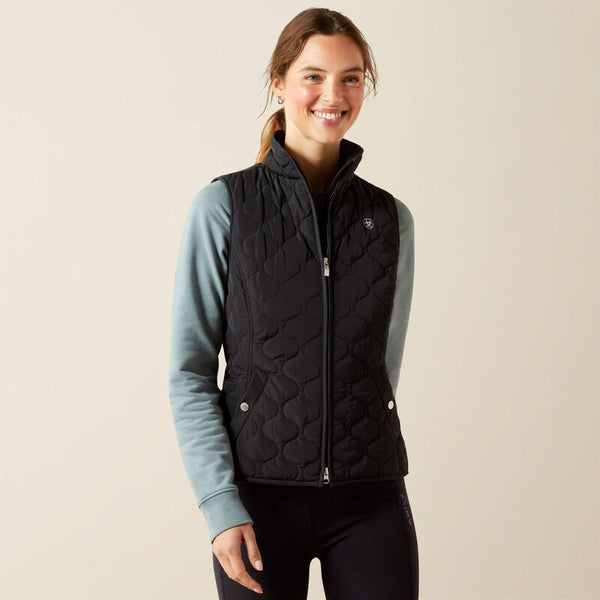 Woman wearing a black quilted vest over a light blue long-sleeve shirt on a beige background