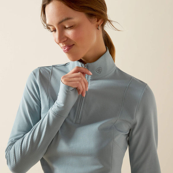 Woman wearing a light blue long-sleeve top with a zipper on a beige background