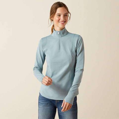 Woman wearing a light blue long-sleeve top with a zipper on a beige background